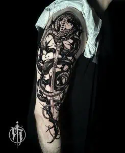 Black and grey snake tattoo with katana sword on the upper arm, showcasing detailed shading and bold lines