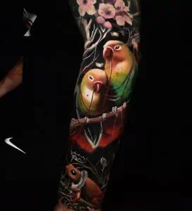 Pink flower tattoo with colourful parrots and vibrant details
